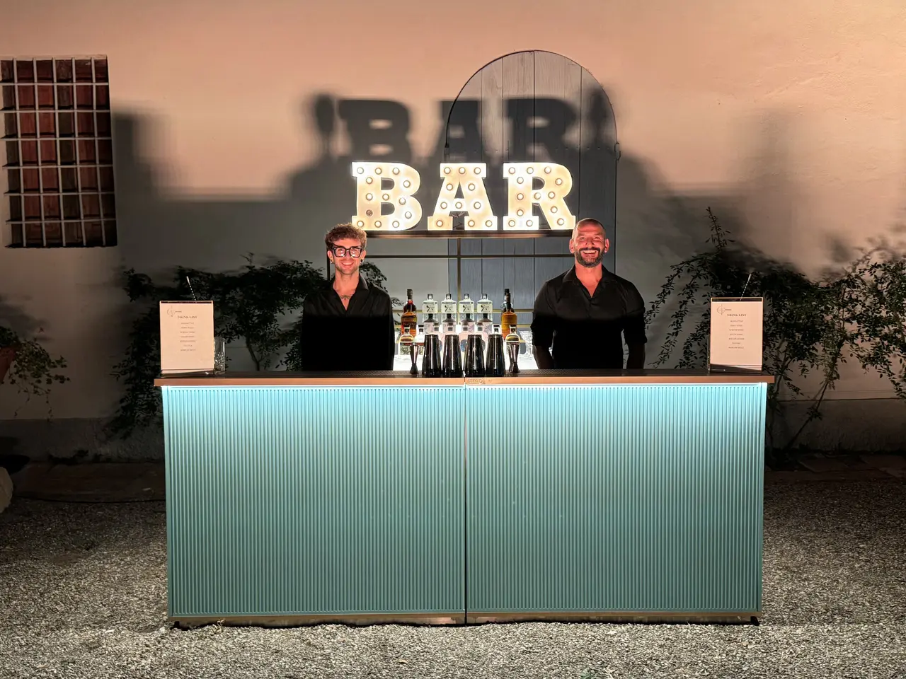 Due bartender dietro il bancone Tiffany azzurro con scritta BAR illuminata.